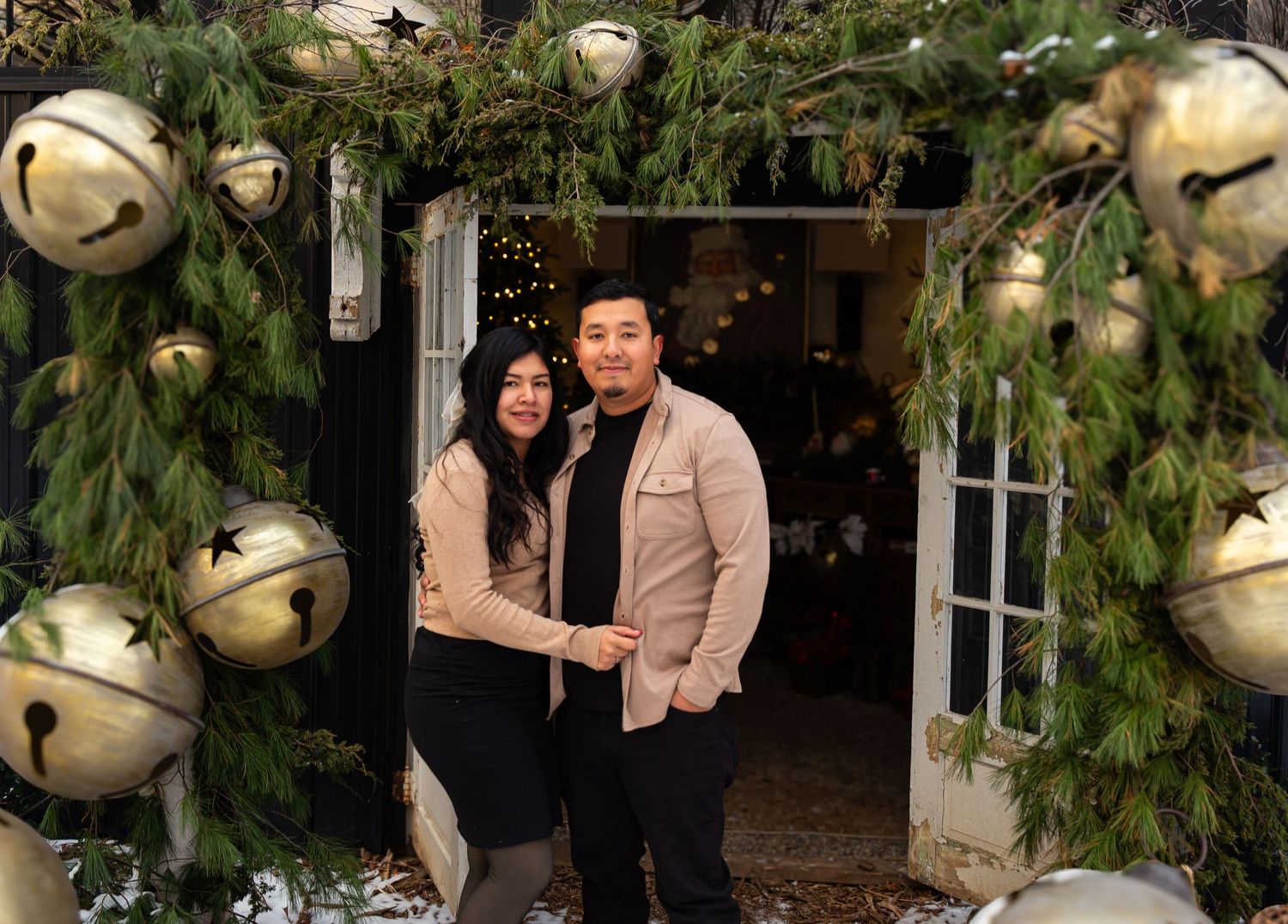 Couple standing in doorway decorated with holiday greenery and large jingle bells.