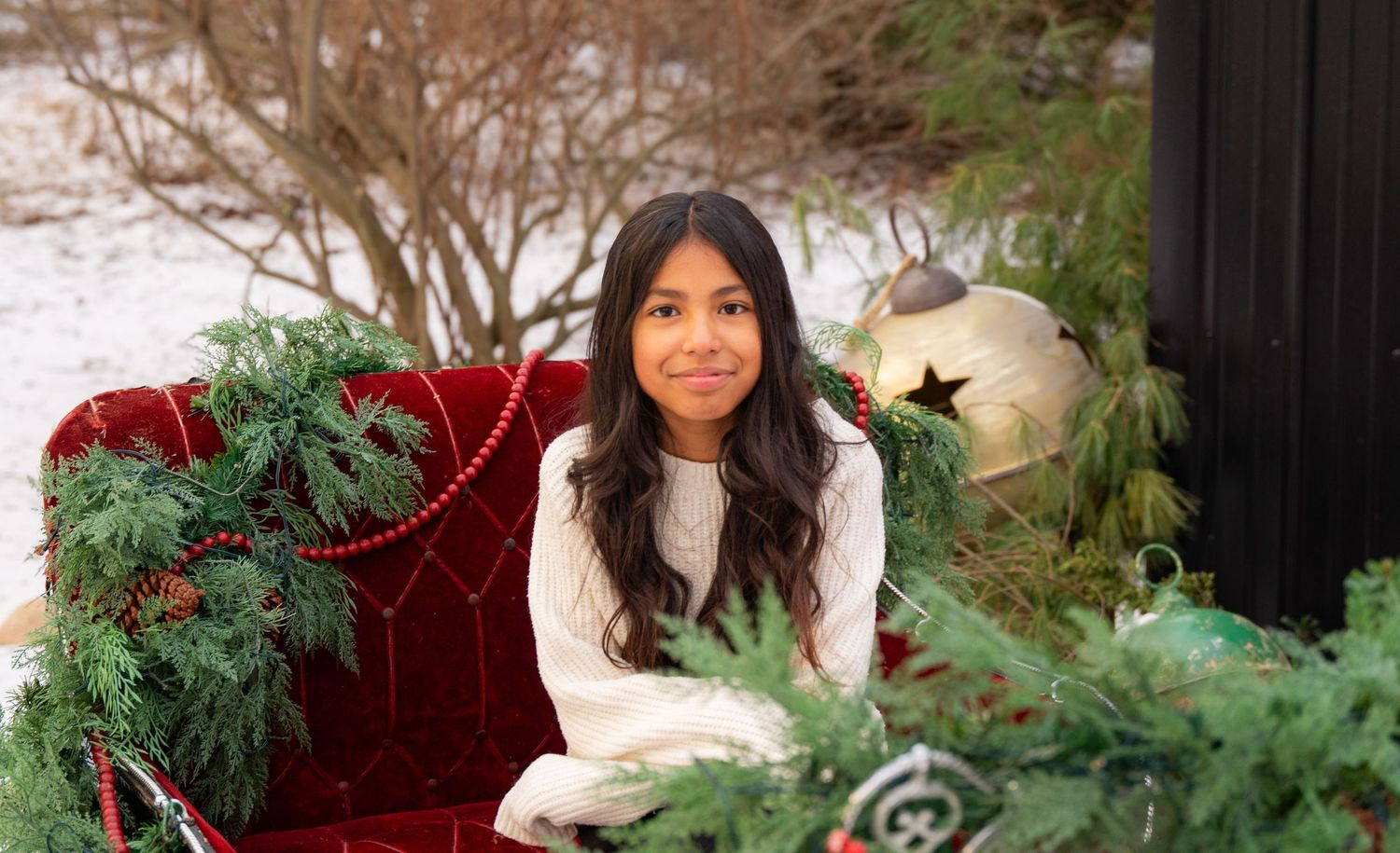 Person sitting on red velvet chair surrounded by holiday greenery and Christmas decorations.