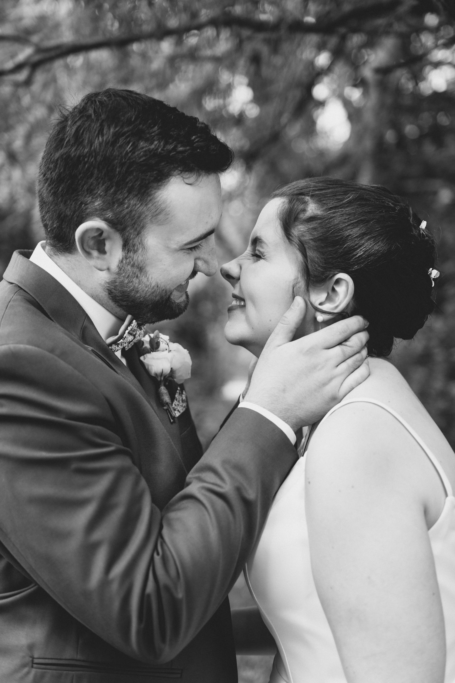 A romantic black and white wedding photo shows a tender moment between newlyweds about to kiss outdoors.