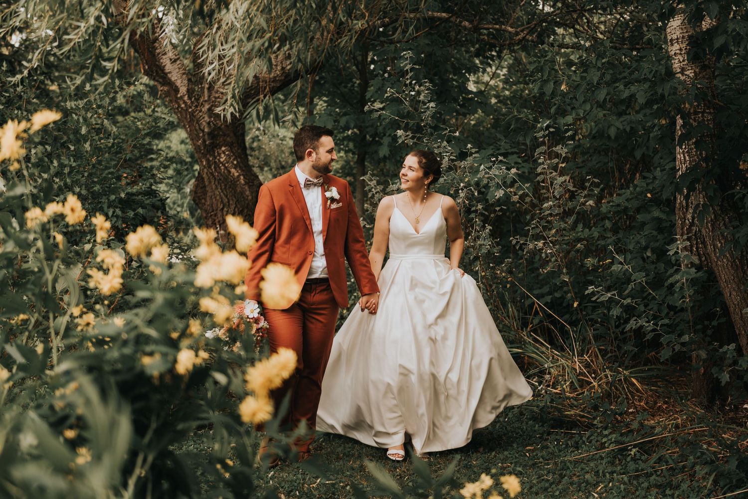 A romantic moment captured in golden sunlight as a couple in wedding attire walks together through a lush garden setting.