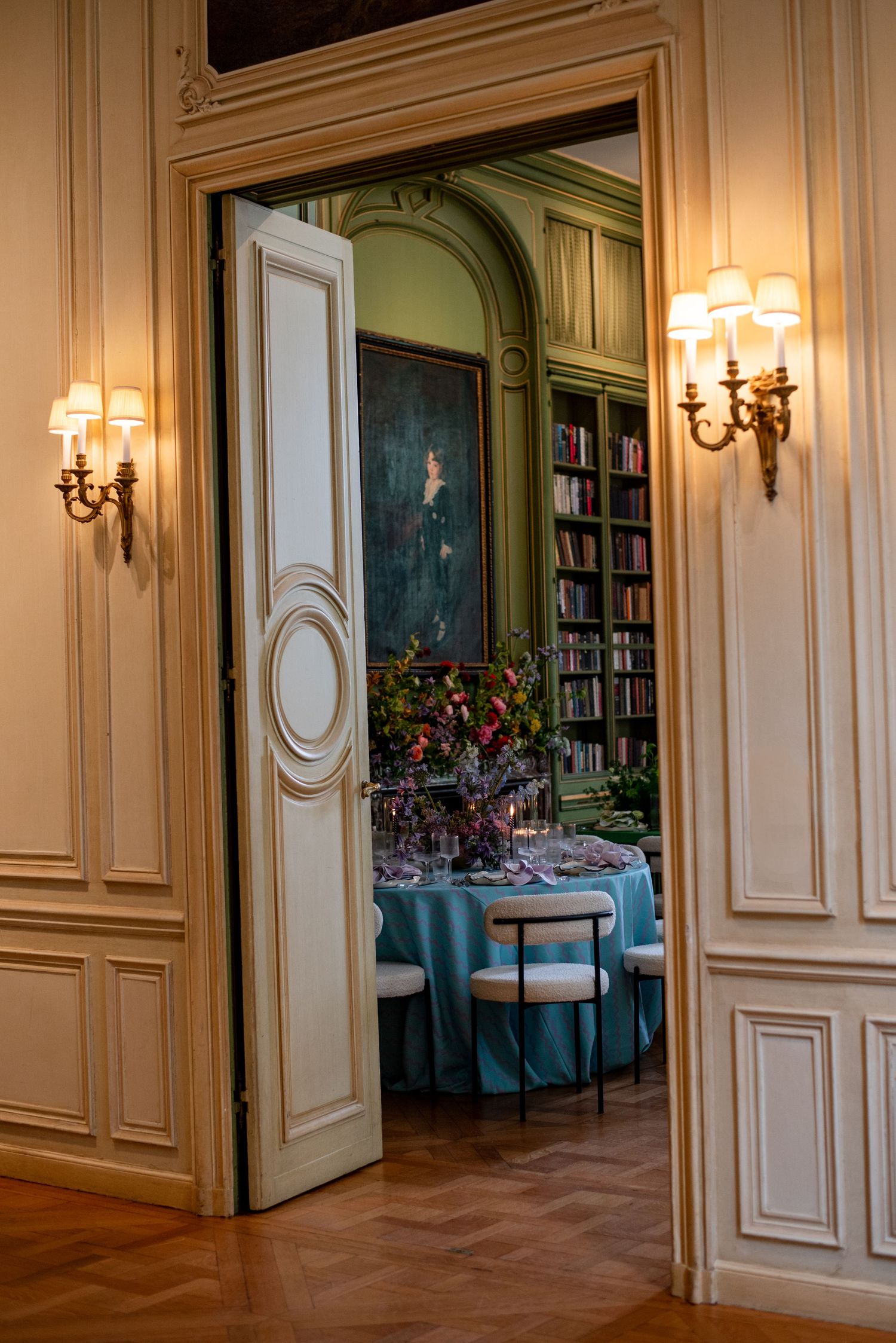 An elegant dining room with blue tablecloths seen through an ornate doorway with wall sconces and wood paneling. Meridian House DC