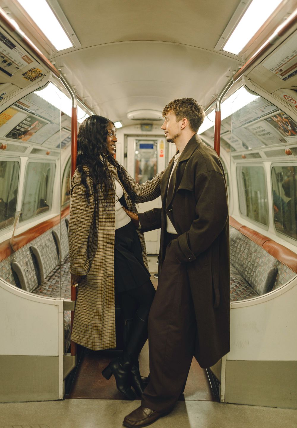 Two people in winter coats share a romantic moment inside an empty subway car.