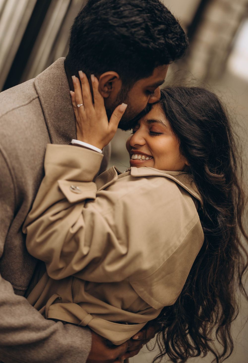 A tender moment between a couple in matching beige coats.