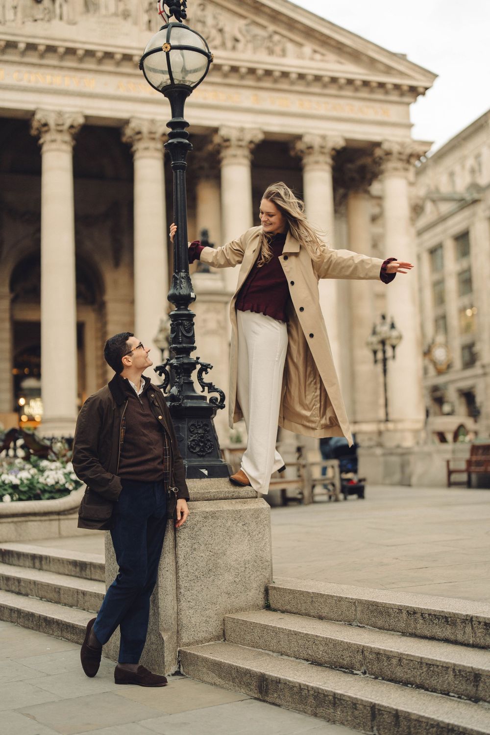 A couple poses playfully on grand stone steps in front of a neoclassical building.