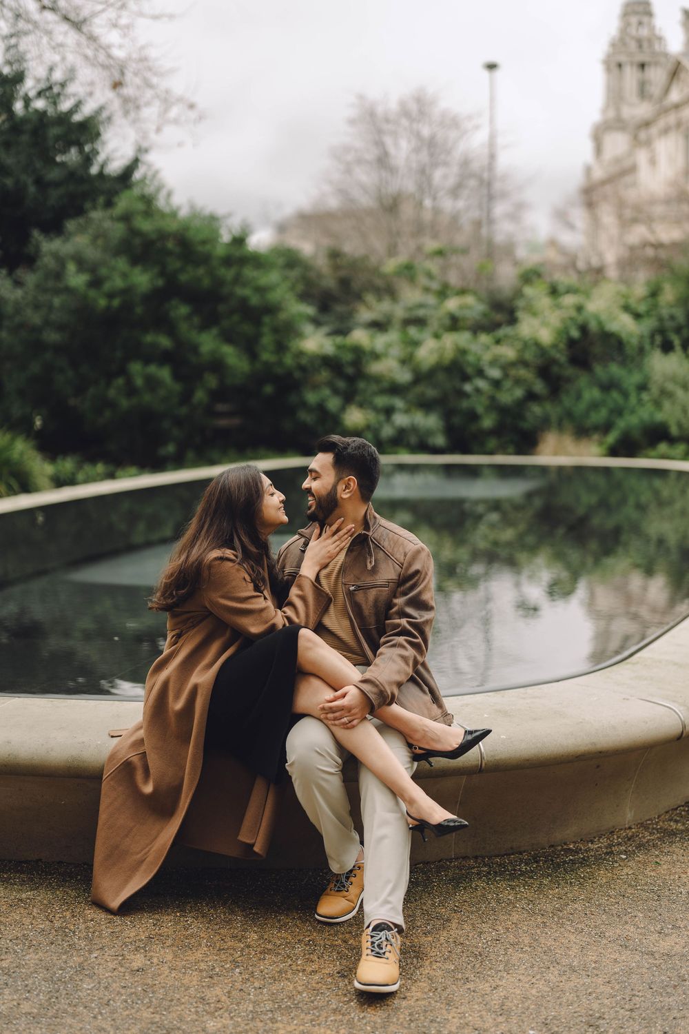 A couple shares romantic moments while sitting on a curved stone bench in a garden setting.