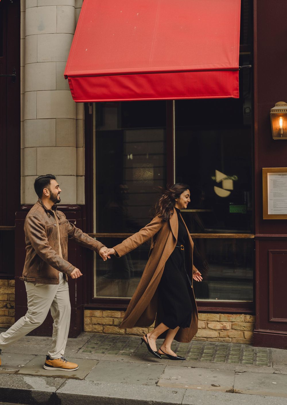 A couple dances together in a playful sequence under a red awning outside a building.