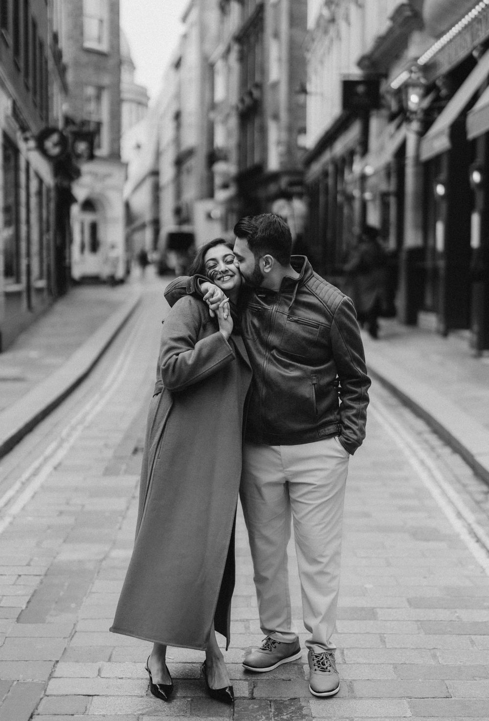 A sequence of black and white photos showing two people hugging and embracing on a cobblestone street.