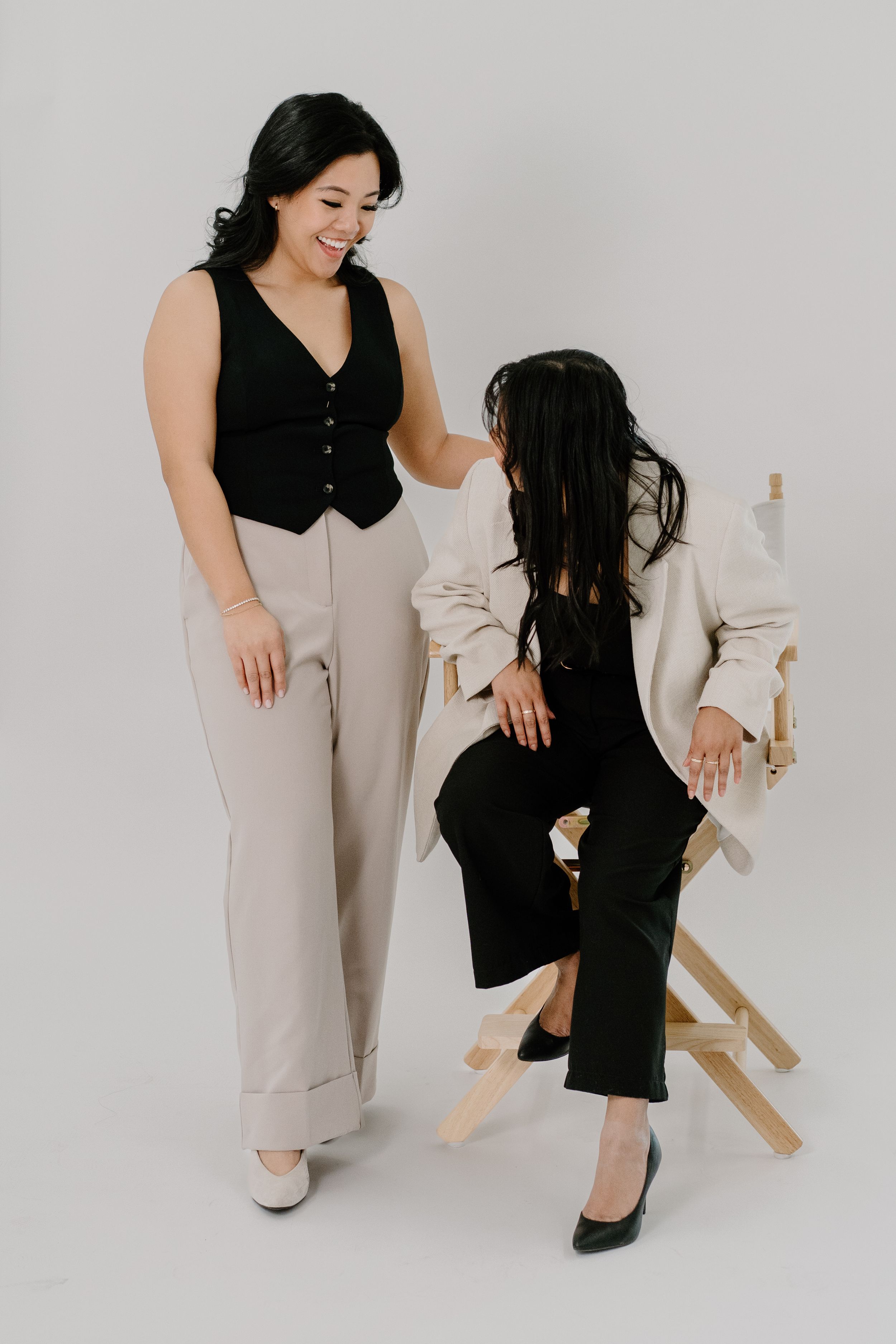 Two people in contrasting black and white business attire pose together in a minimalist studio setting.