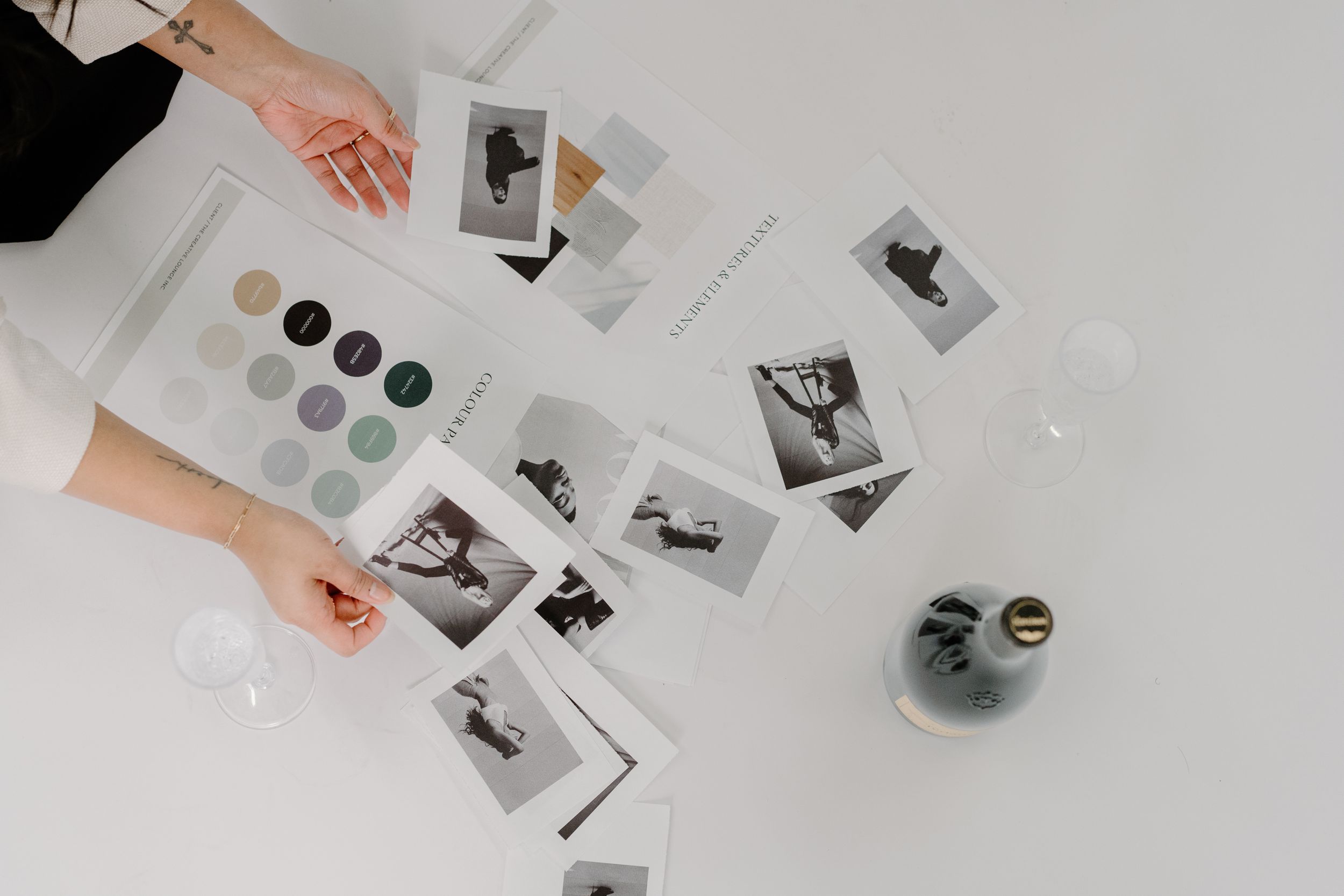 Hands arranging black and white photographs and color swatches on a white surface next to a glass vase.