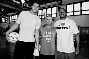 Three basketball players pose together in a gym, with one holding a ball and another wearing a 'Haters!' t-shirt.