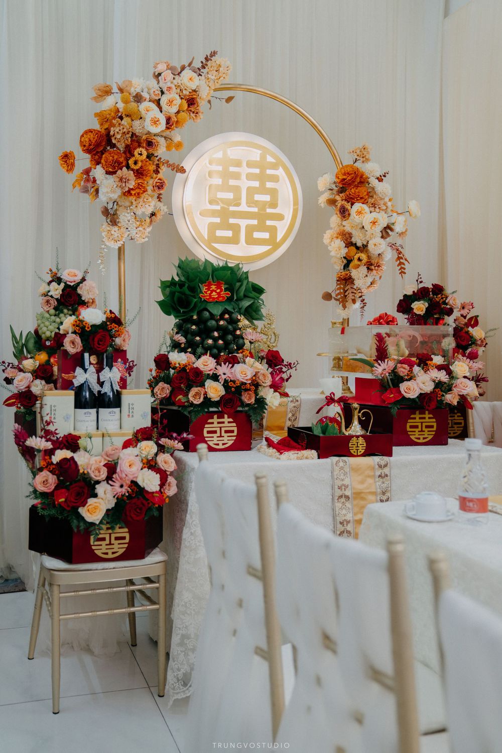 Traditional Chinese double happiness wedding decor with floral arrangements and illuminated gold arch backdrop.