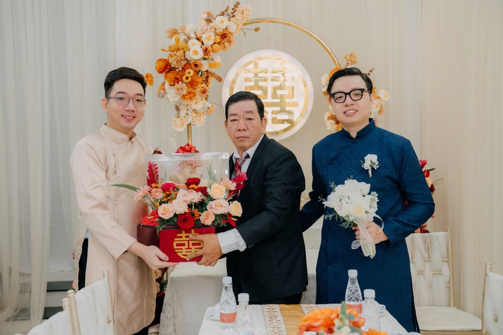 Three men pose with a decorative wedding cake at a traditional Chinese Vietnamese wedding ceremony.