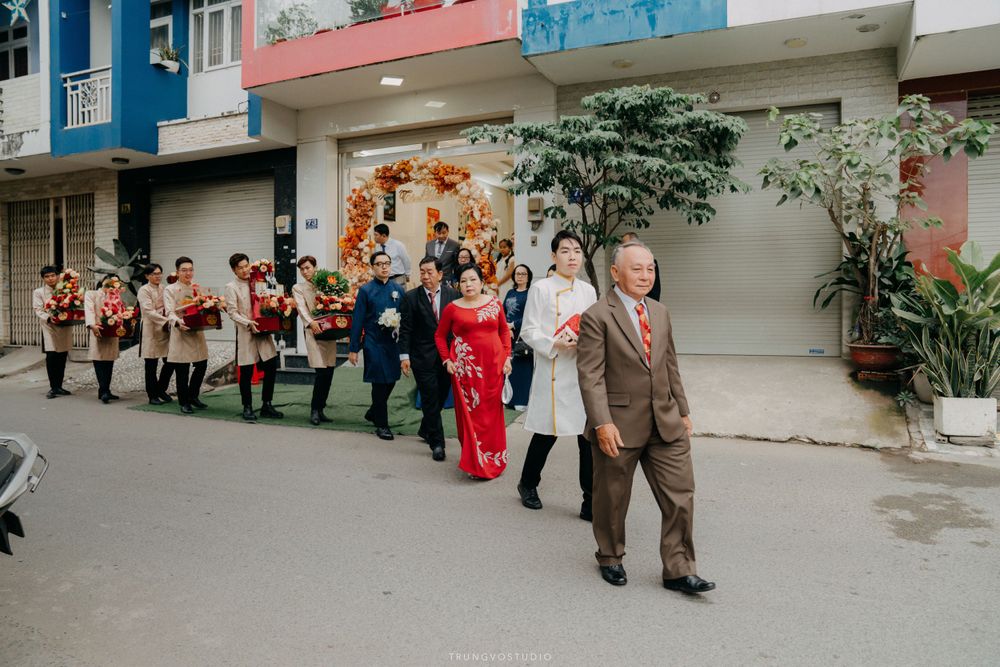 Wedding procession walks down street with floral arrangements at traditional Vietnamese ceremony.