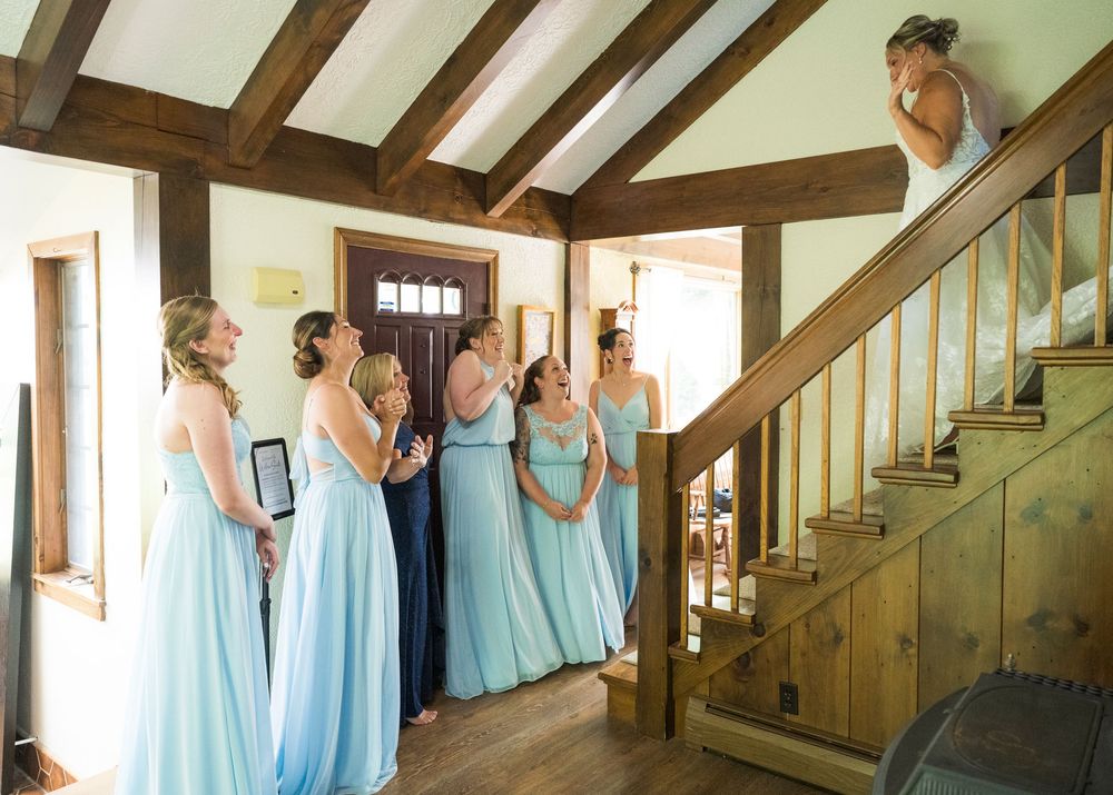 A group wearing matching light blue dresses prepares in a rustic wooden hallway with exposed beams and natural light.