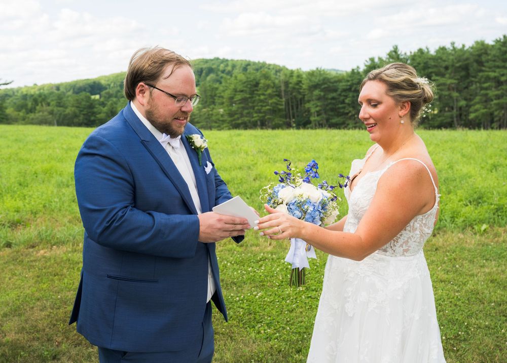 A couple pops a champagne bottle together in a grassy field during their wedding celebration.