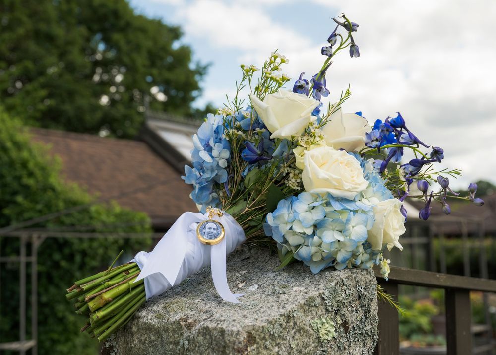 Wedding bouquet with white roses and blue flowers resting on a stone surface.