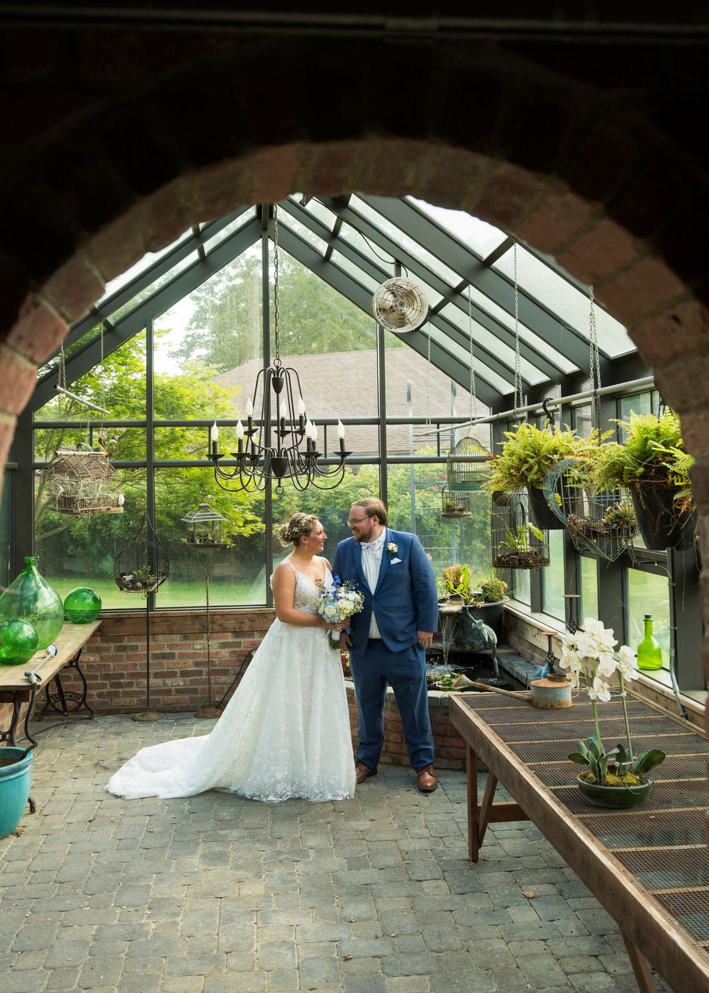 Wedding ceremony takes place in a rustic greenhouse venue with stone floors and hanging plants.