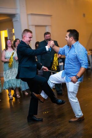 Two guests performing an energetic dance move on a dark wooden floor at a wedding reception.