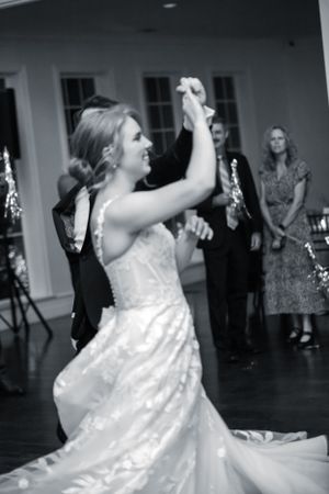 A flowing white wedding dress twirls gracefully during a dance on a dark wooden floor.