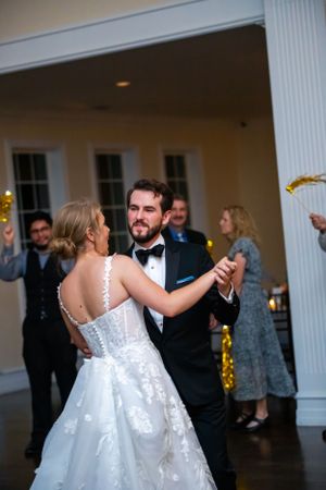 Wedding couple dances inside a columned venue with guests watching in background.