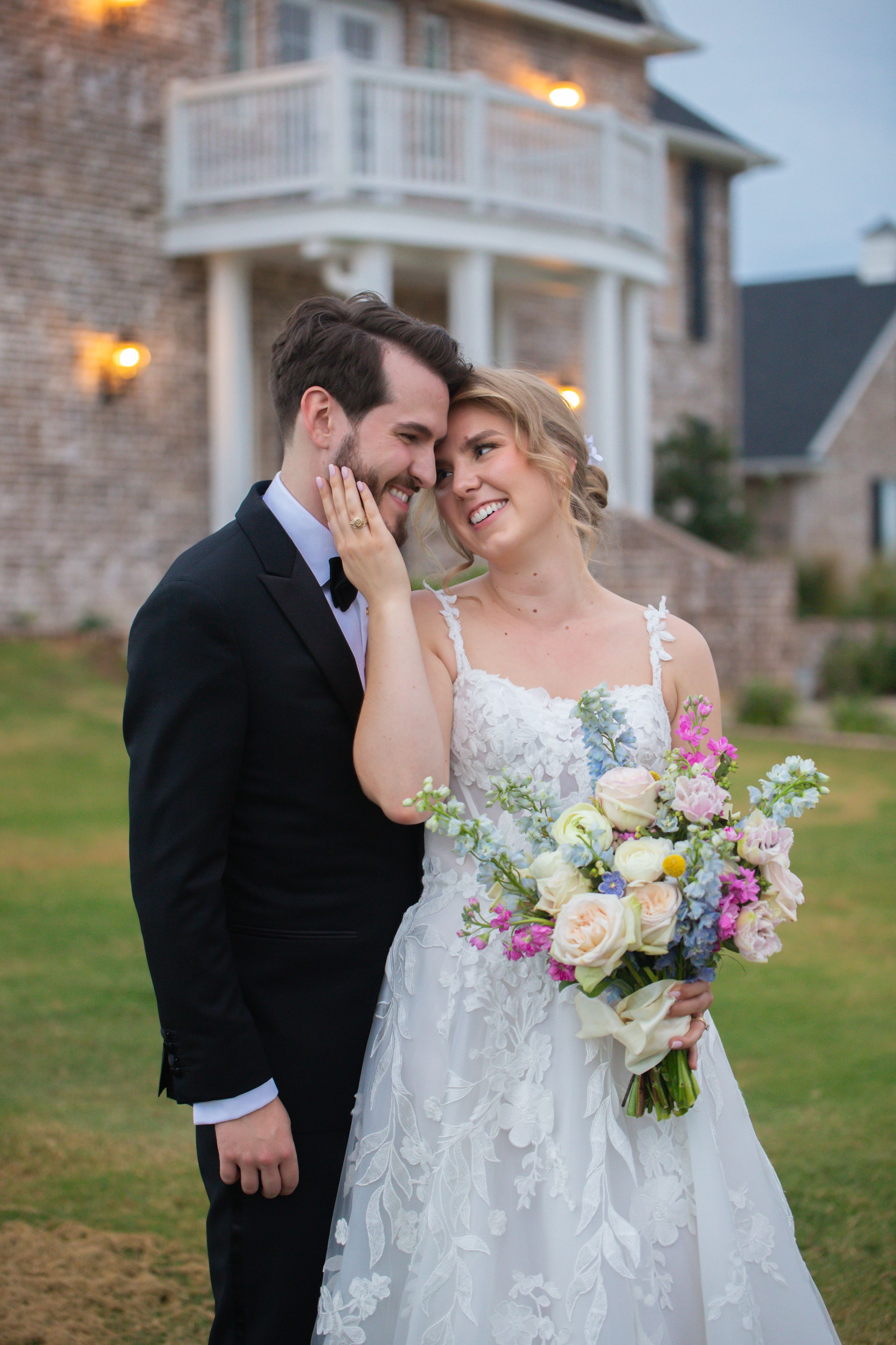 Romantic outdoor wedding portrait with a colorful bouquet against brick architecture.