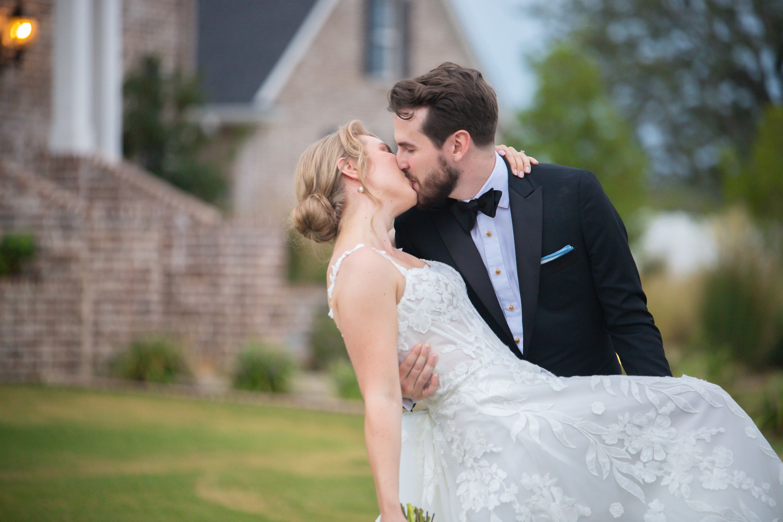 Newlyweds share a romantic moment outdoors against a brick building backdrop.