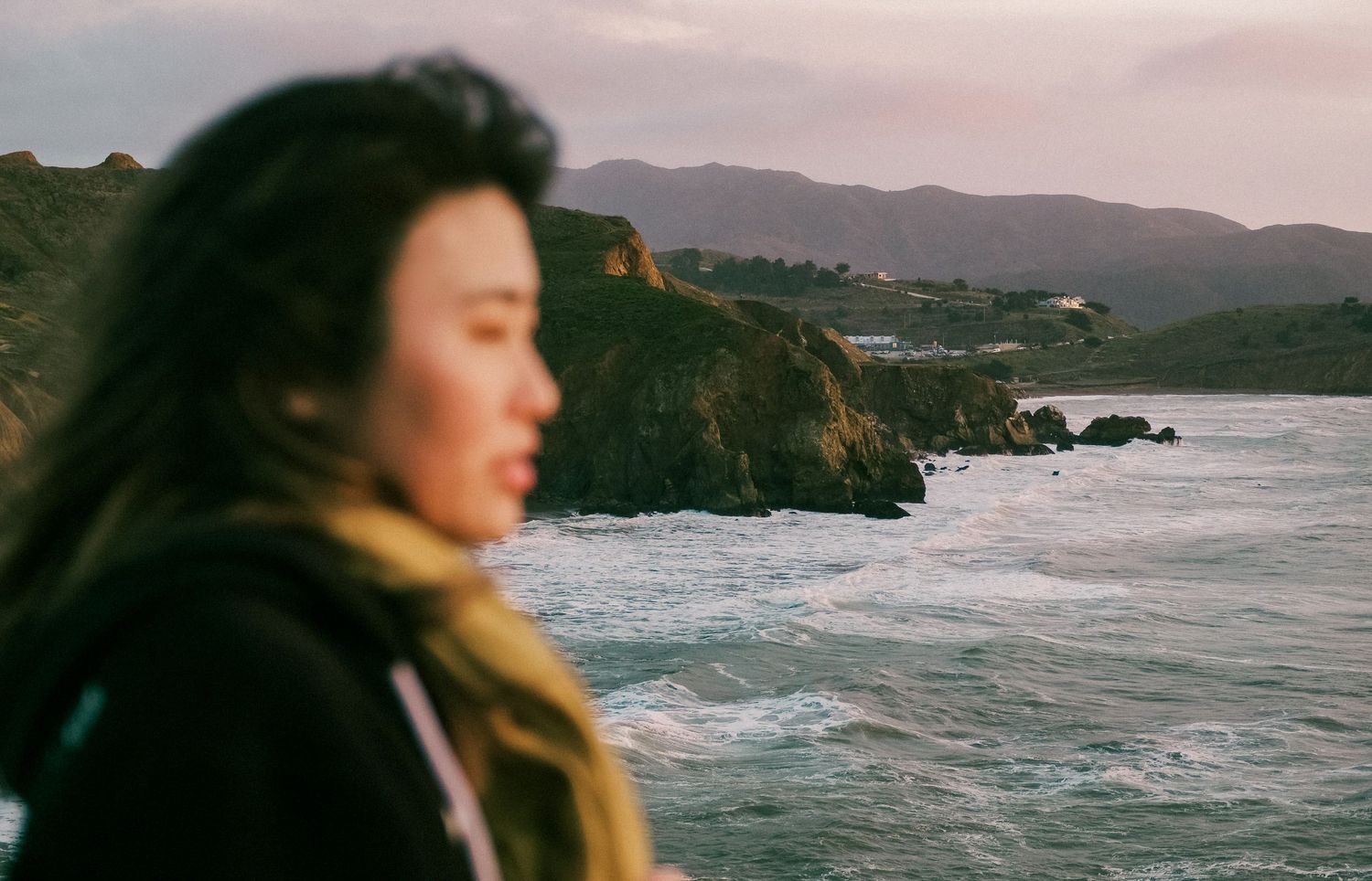 Person gazing at dramatic coastal cliffs and ocean waves during sunset.
