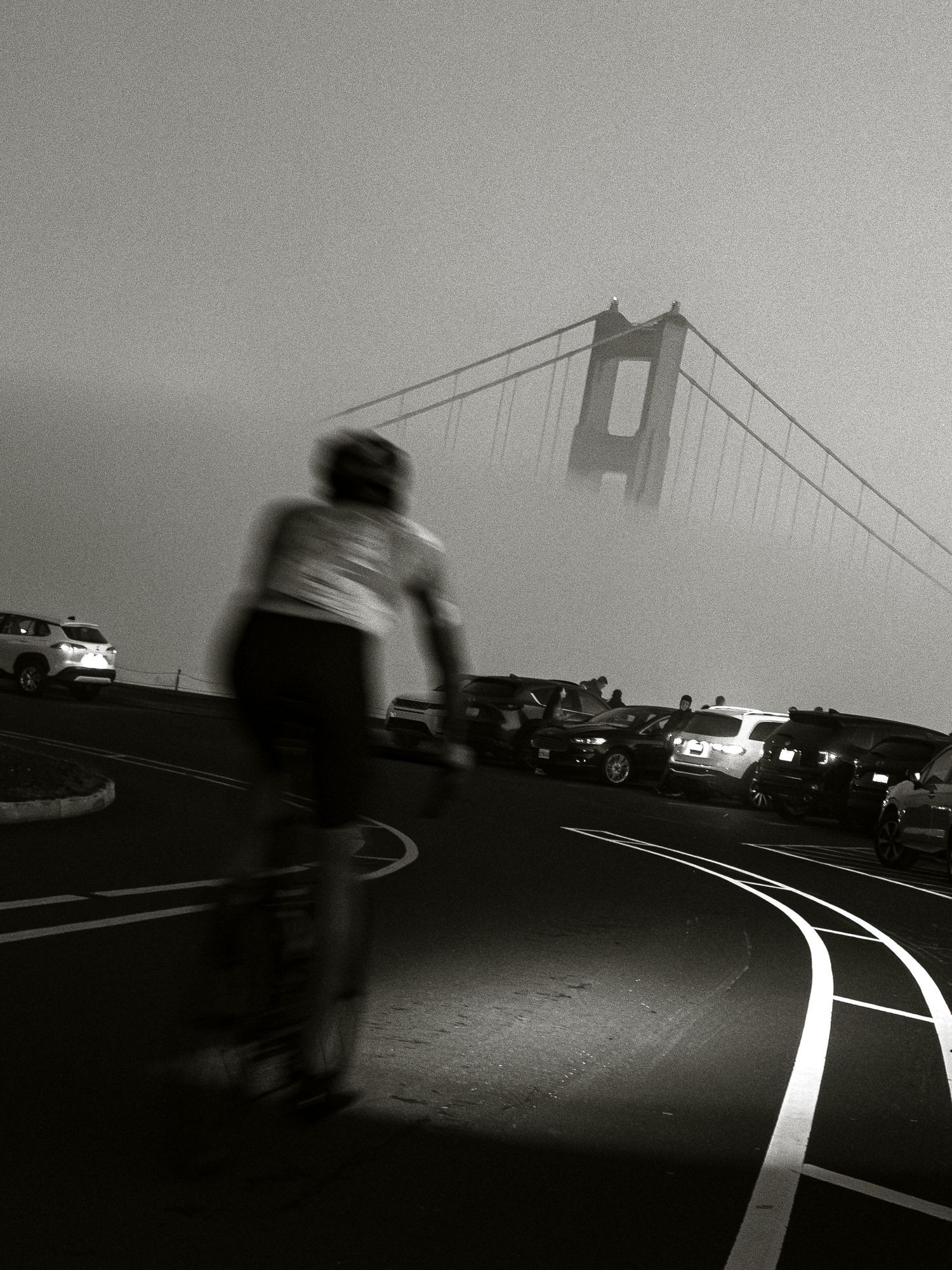 Silhouette of cyclist near Golden Gate Bridge emerging through fog in dramatic black and white composition.