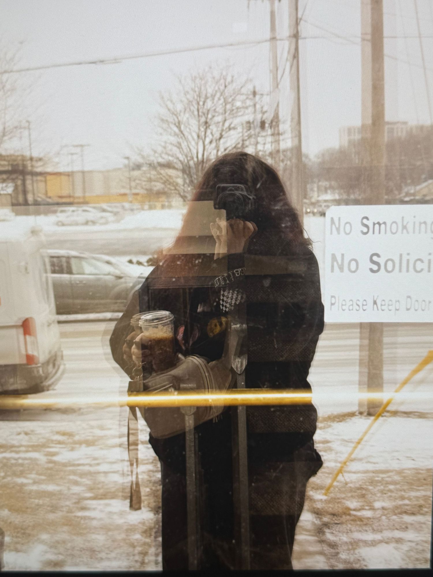 A vintage-style photograph through glass shows a reflection with a 'No Smoking' sign visible in winter conditions.