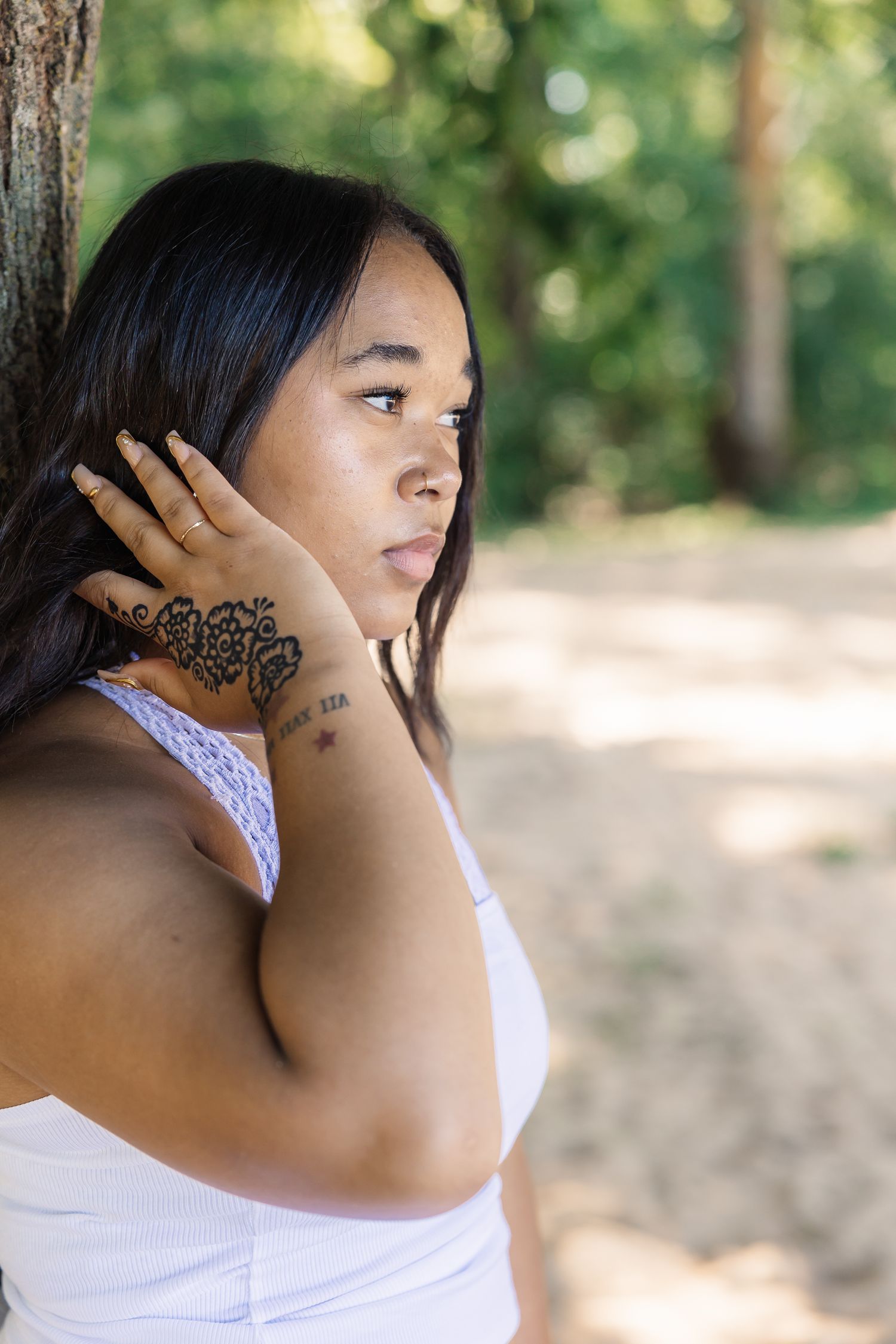 A person in white touches their neck while posing against a natural outdoor background.