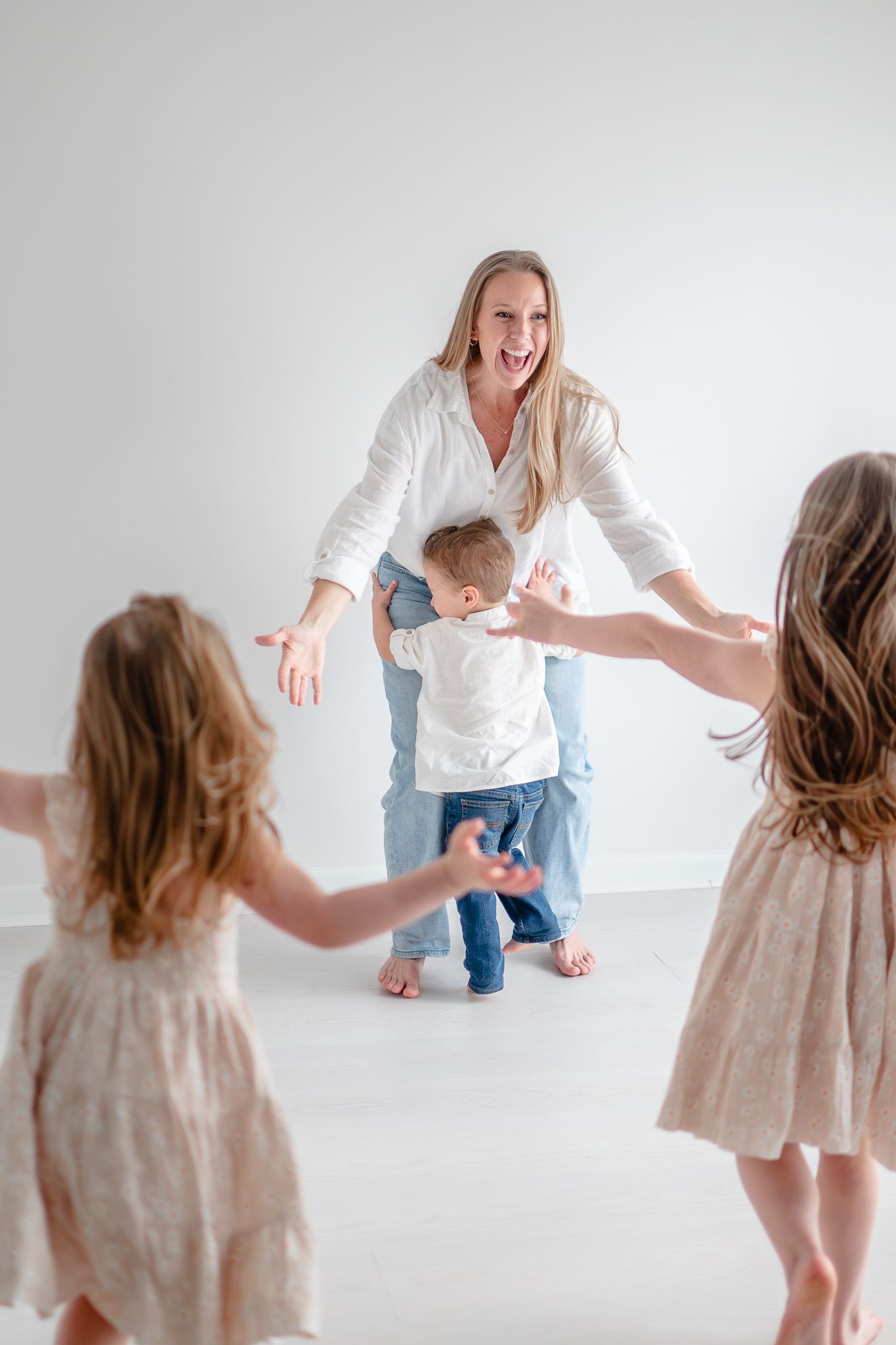 A playful family moment captured in a bright white studio as they dance and laugh together.
