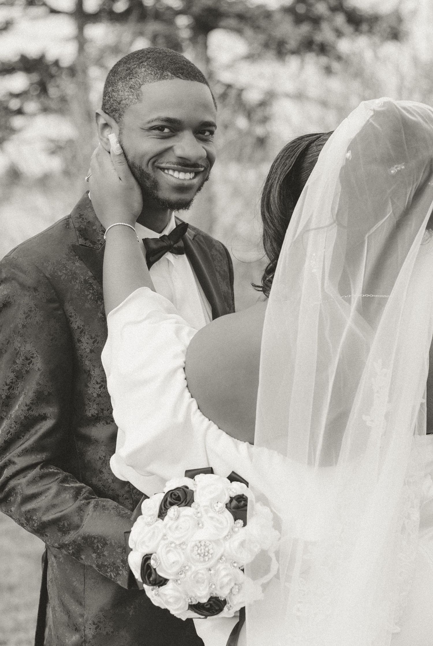 Black and white wedding photo of a tender moment between newlyweds, with bride holding white rose bouquet.