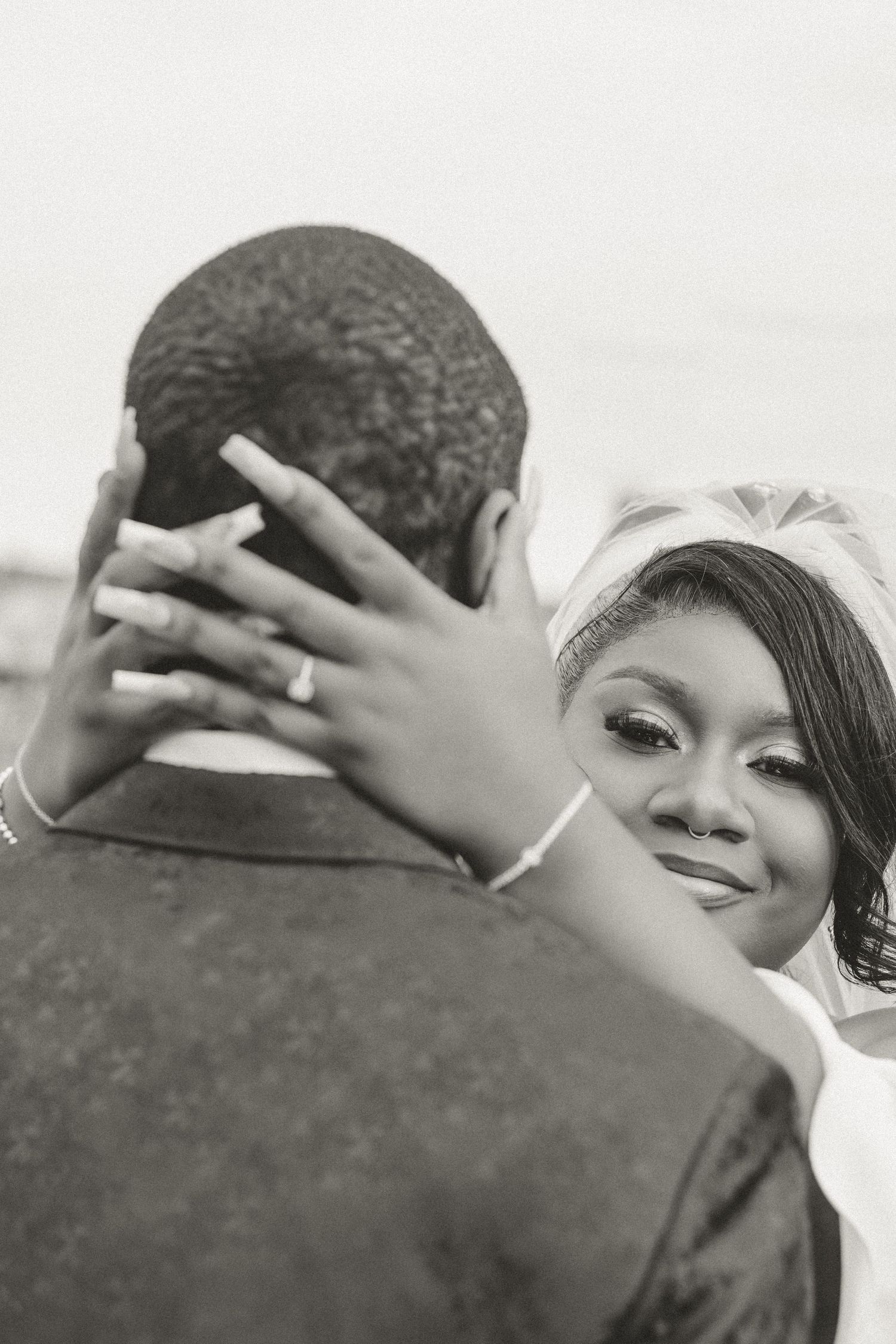 A black and white wedding photo showing an intimate moment between a bride and groom embracing outdoors.