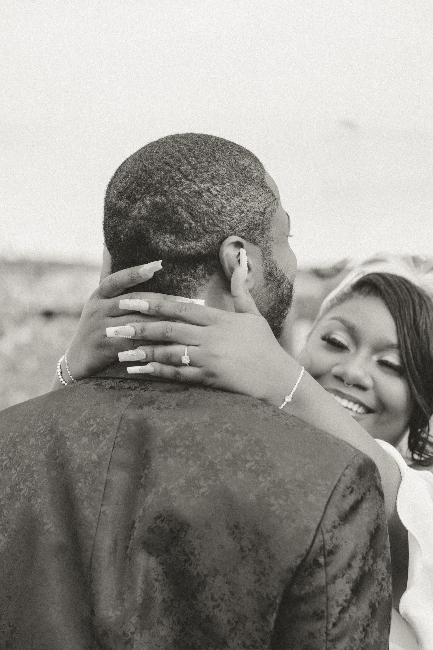 An intimate black and white photo of a couple embracing, with hands gently placed around the back of the neck.