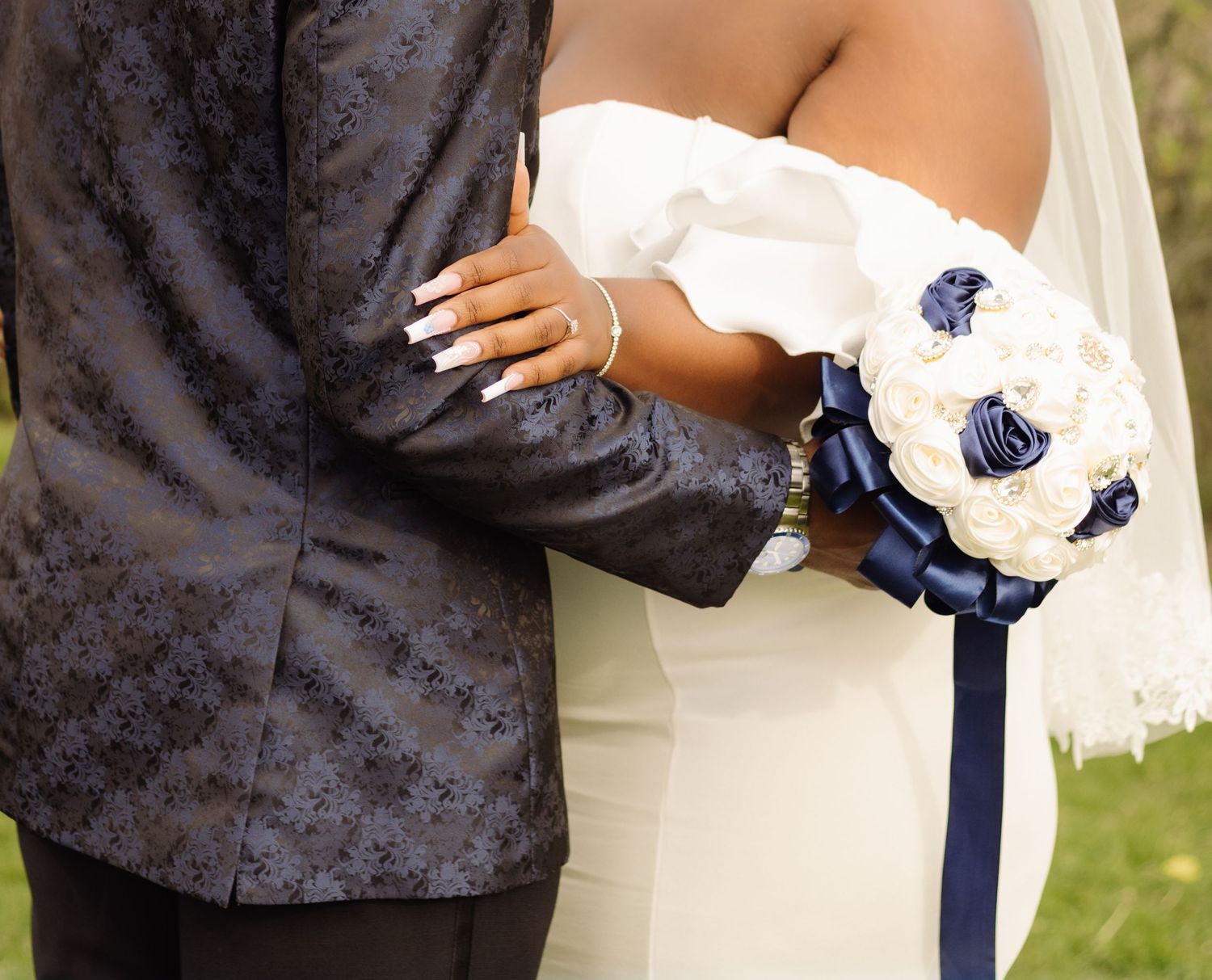 A bride and groom hold each other close, with the bride's bouquet featuring white and navy blue flowers.