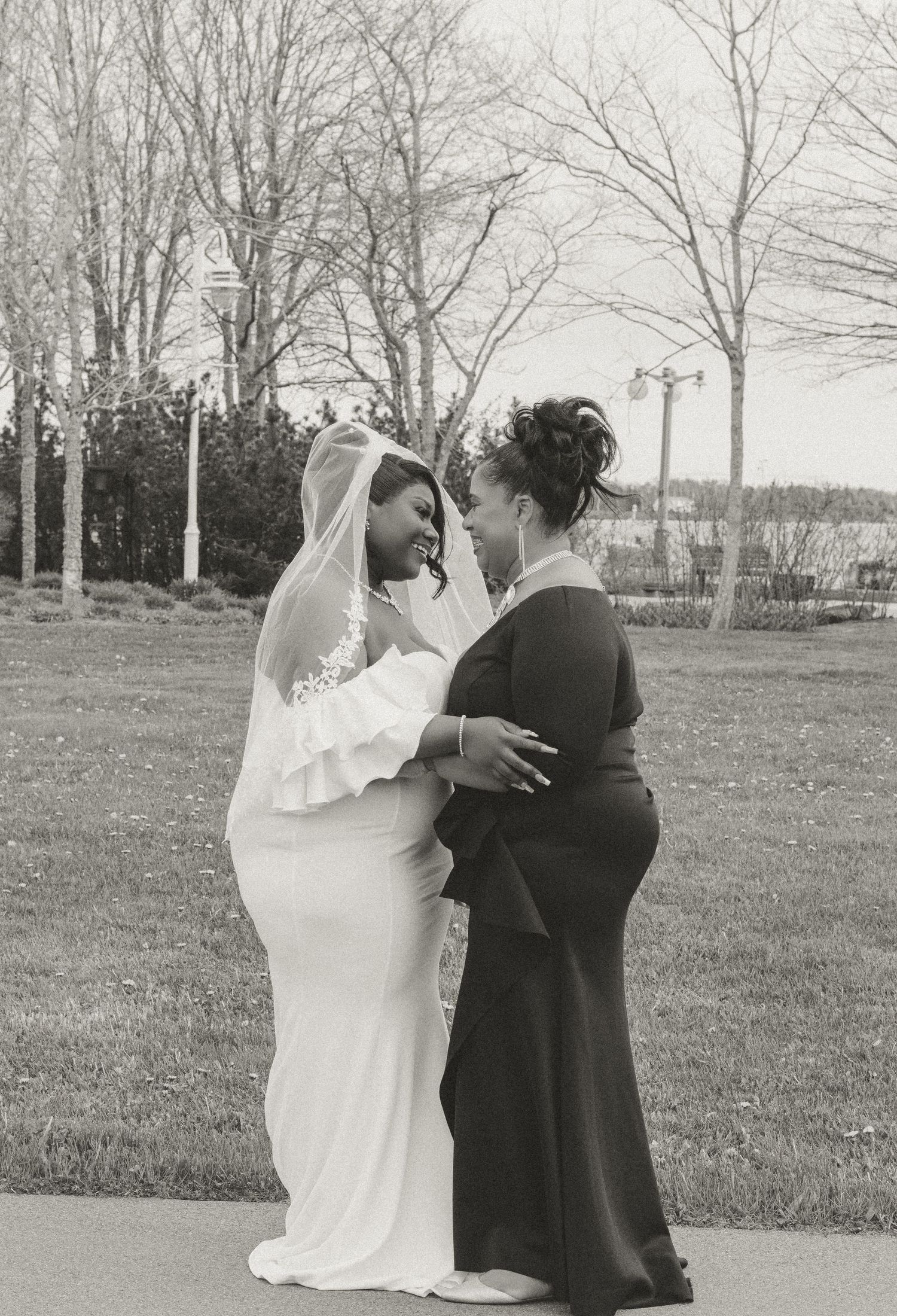 A bride in white and companion in black share an intimate moment together outdoors on their wedding day.