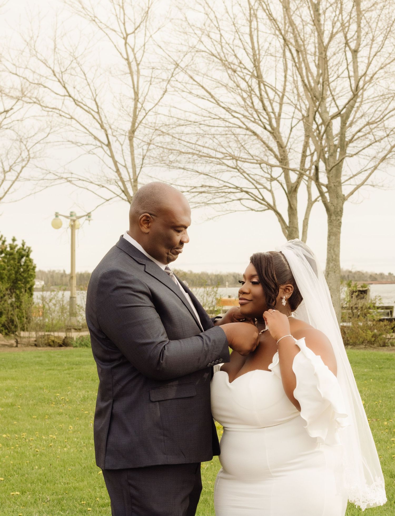 A wedding couple share a tender moment together outdoors with bare trees in the background.