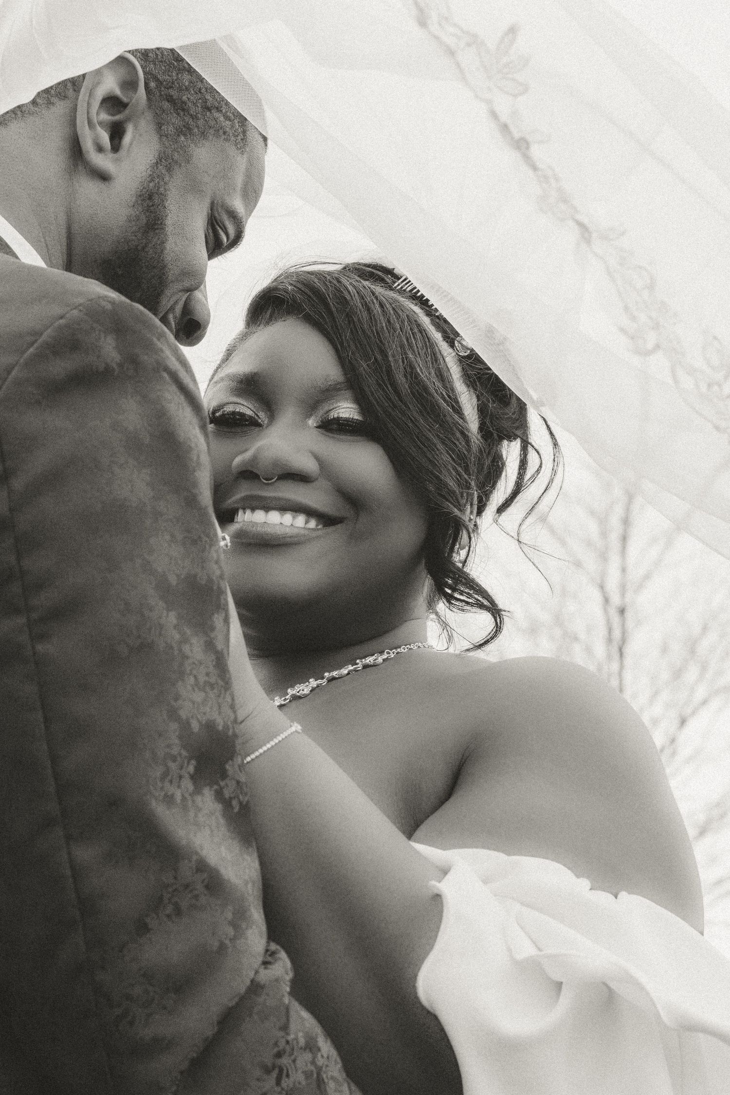 A joyful black and white portrait of newlyweds sharing an intimate moment with delicate jewelry details.