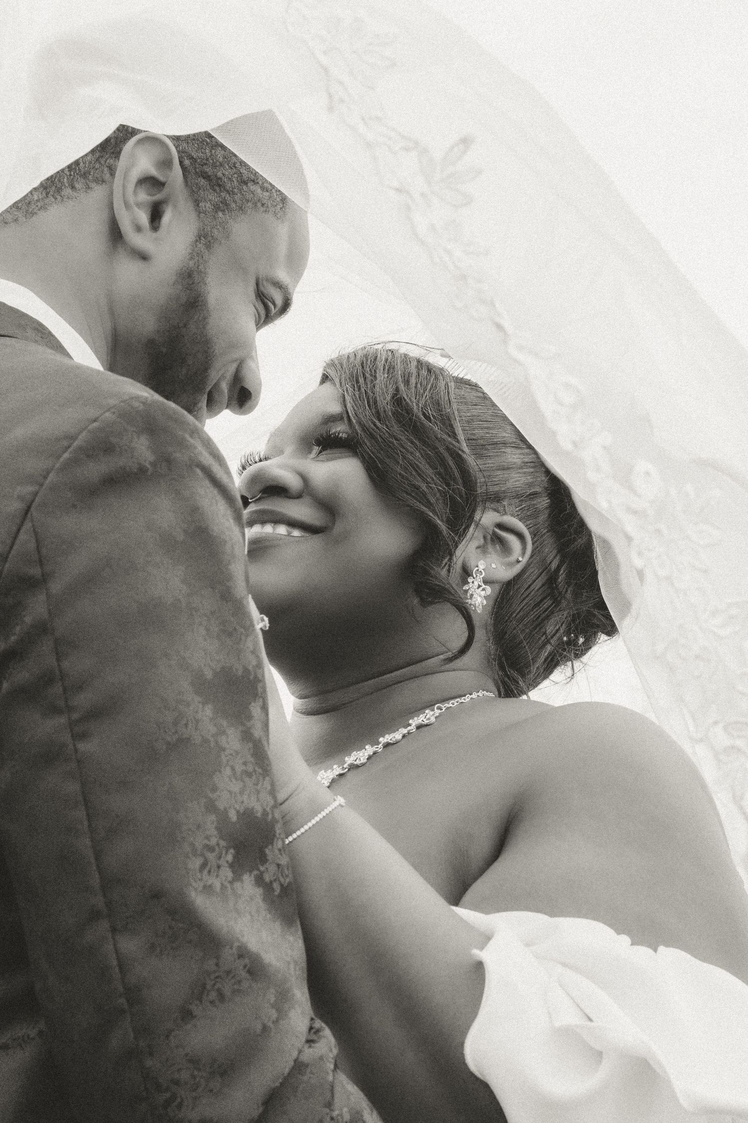 Intimate black and white wedding photo showing a romantic moment between newlyweds in formal attire.