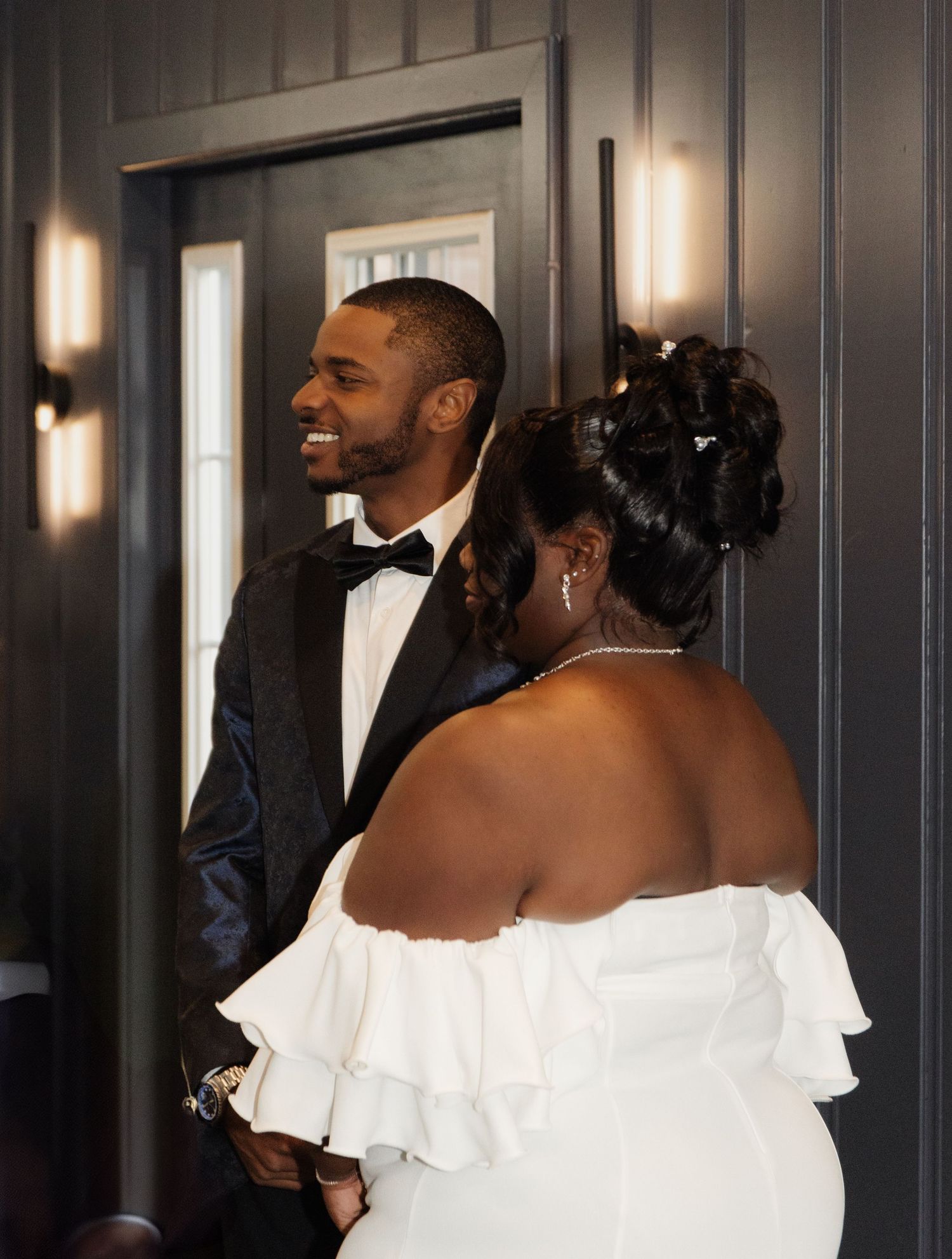 A wedding couple sharing joyful smiles in an elegantly lit hallway.