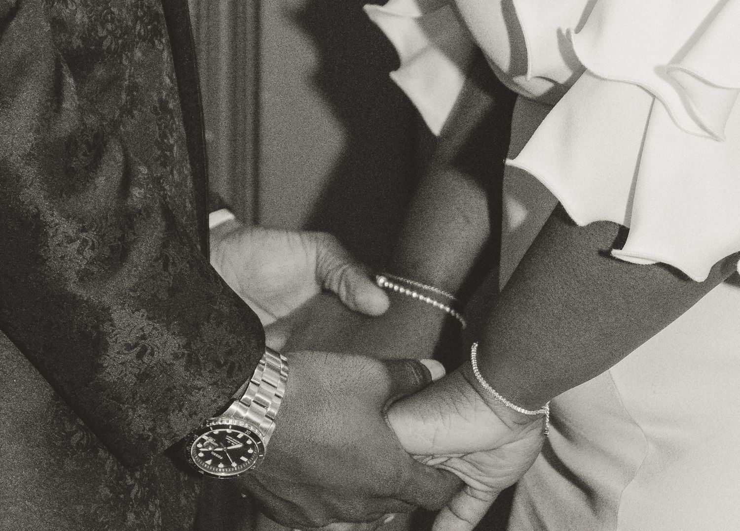 A close-up black and white photograph shows hands checking a medical bracelet or ID band in a clinical setting.