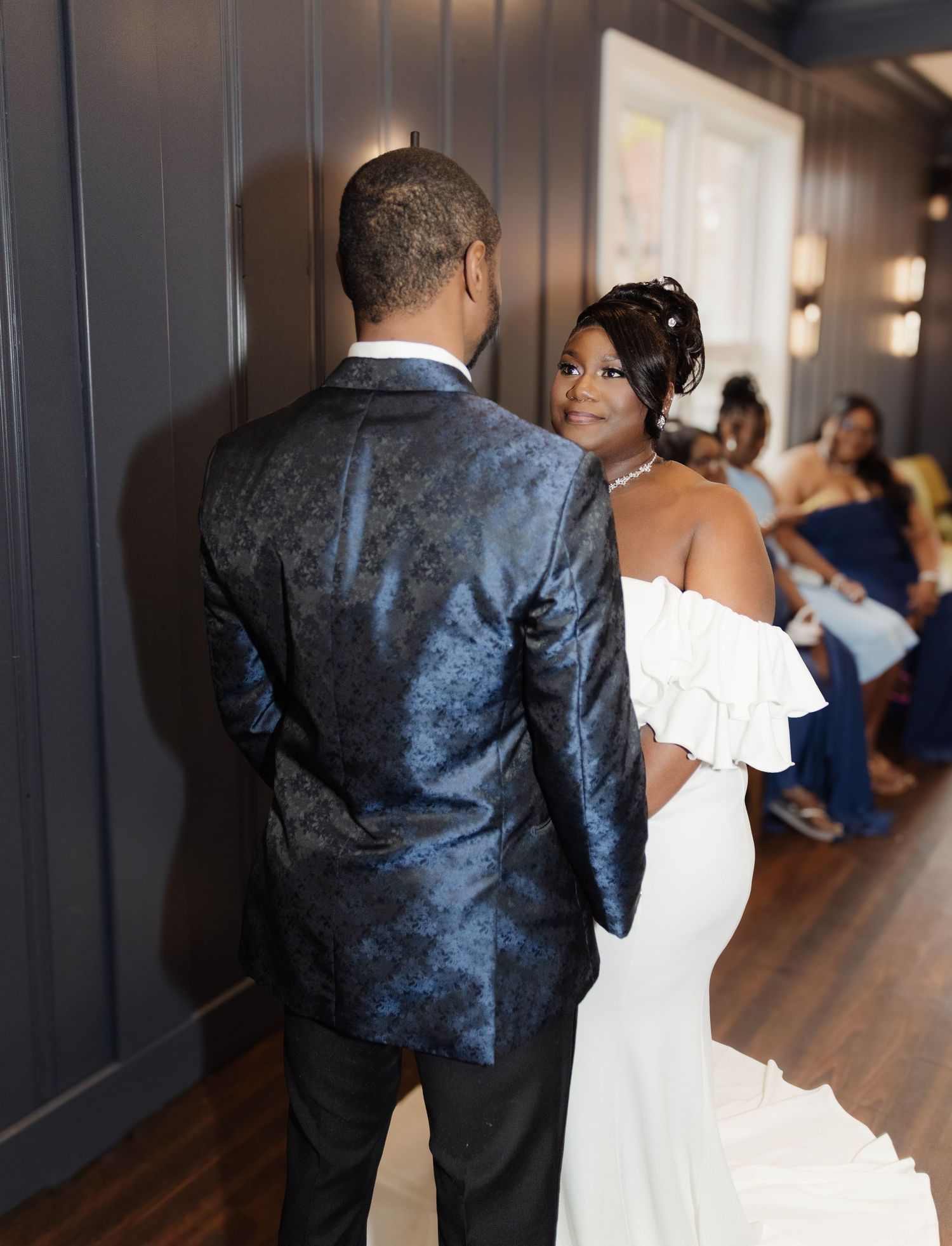 Elegant couple at a wedding captured in an intimate moment in a hallway with dark walls and hardwood floors.