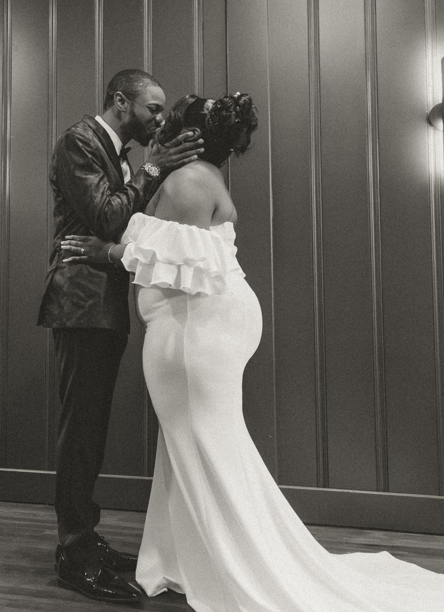 Romantic black and white portrait of couple in wedding attire sharing an intimate moment indoors.