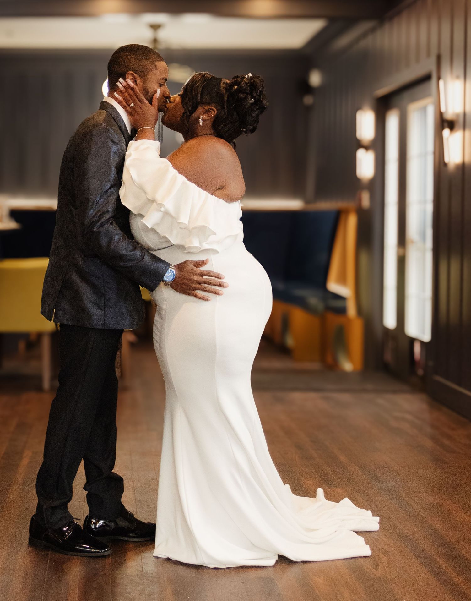 Intimate wedding moment as couple embraces on hardwood floor with bride wearing stunning white mermaid gown.