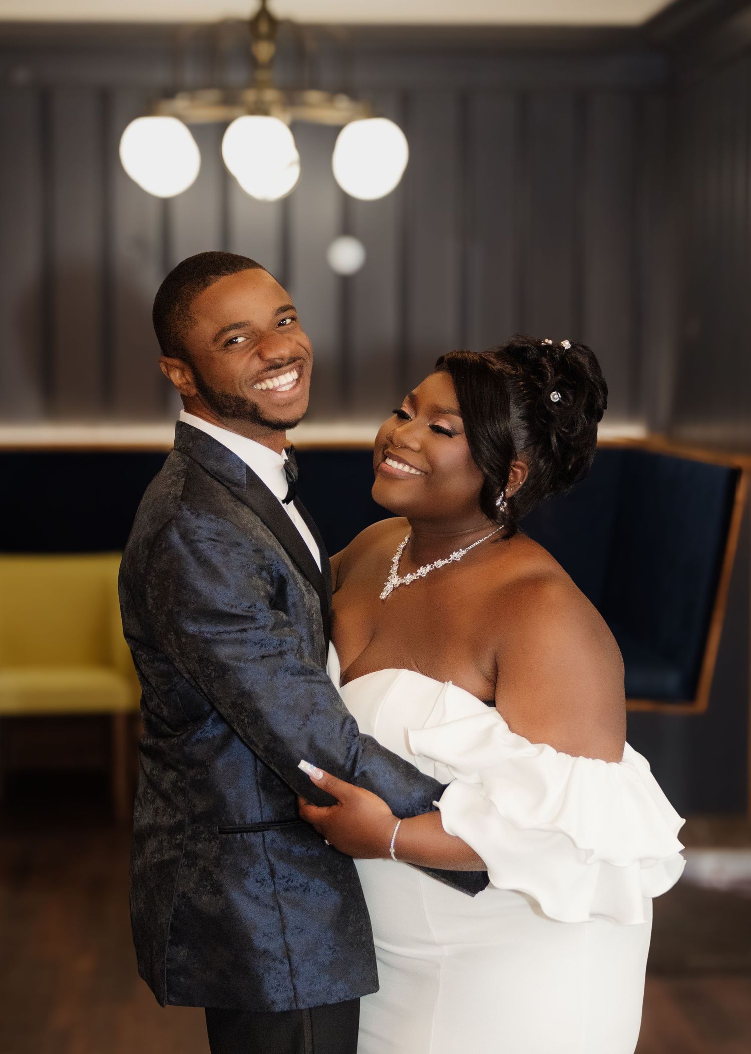 A happy couple embraces and smiles during their wedding celebration in an elegantly lit venue.