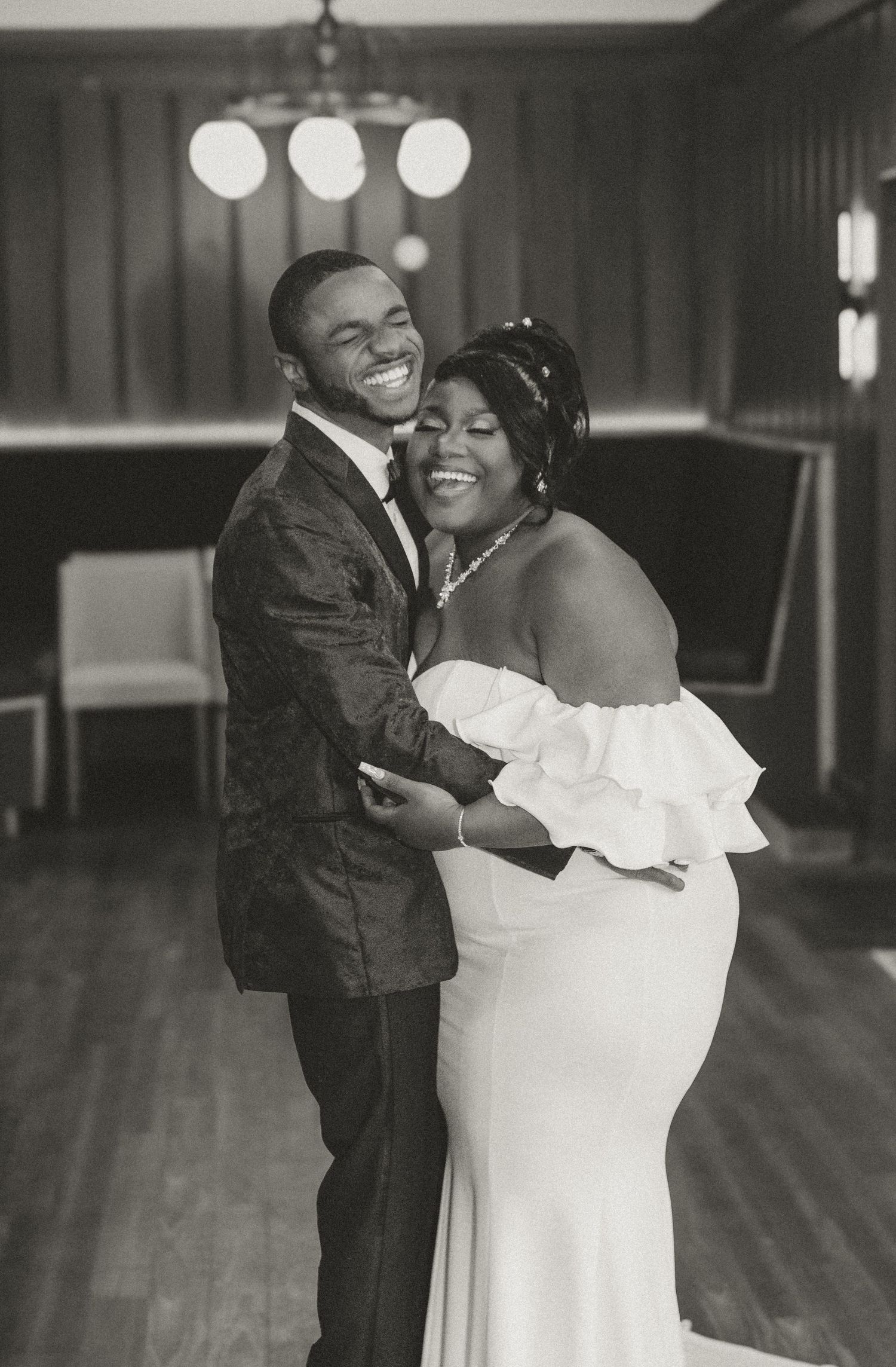 Black and white photo of newlyweds embracing and laughing during their wedding reception.