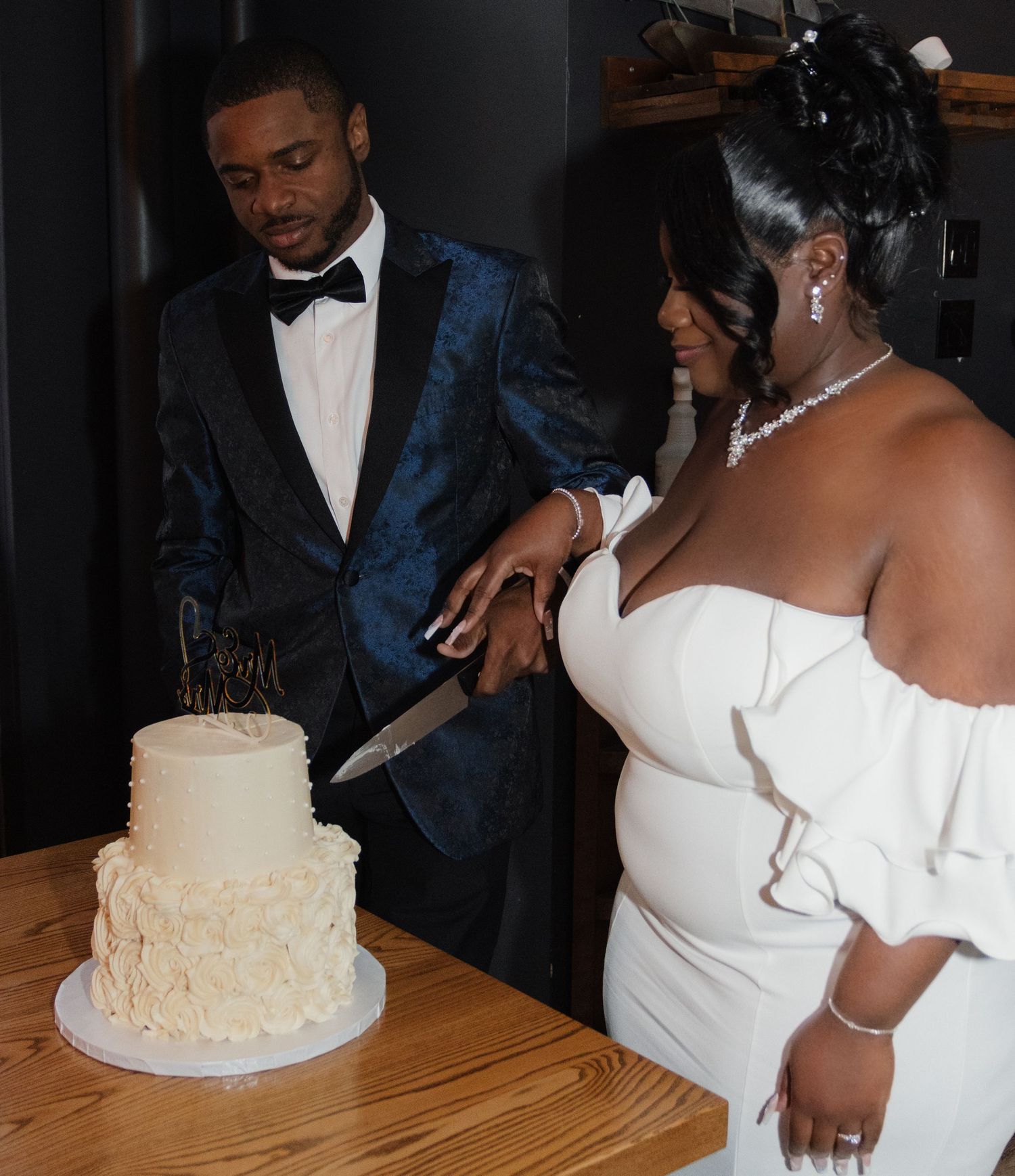 A couple in formal wedding attire prepare to cut their elegant white wedding cake together.