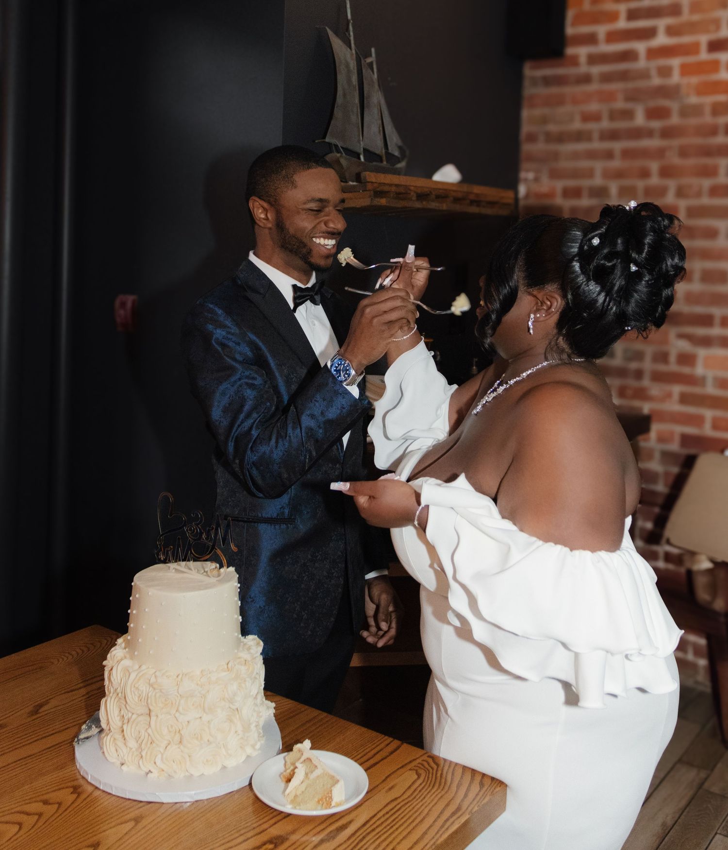 Wedding couple sharing cake during traditional cake cutting ceremony in rustic venue.