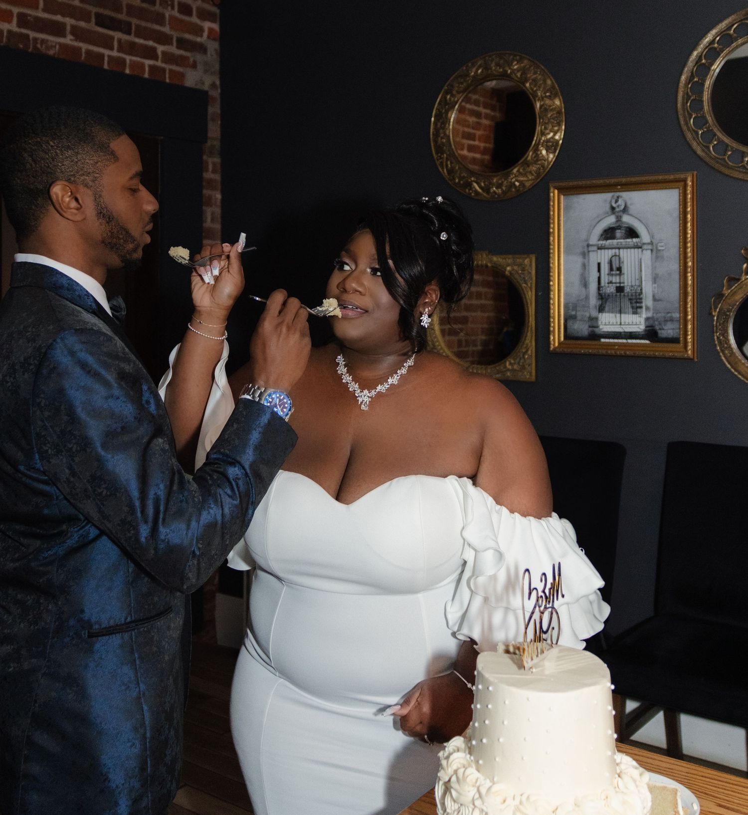 A couple shares a special moment while cutting their elegant white wedding cake adorned with gold accents.