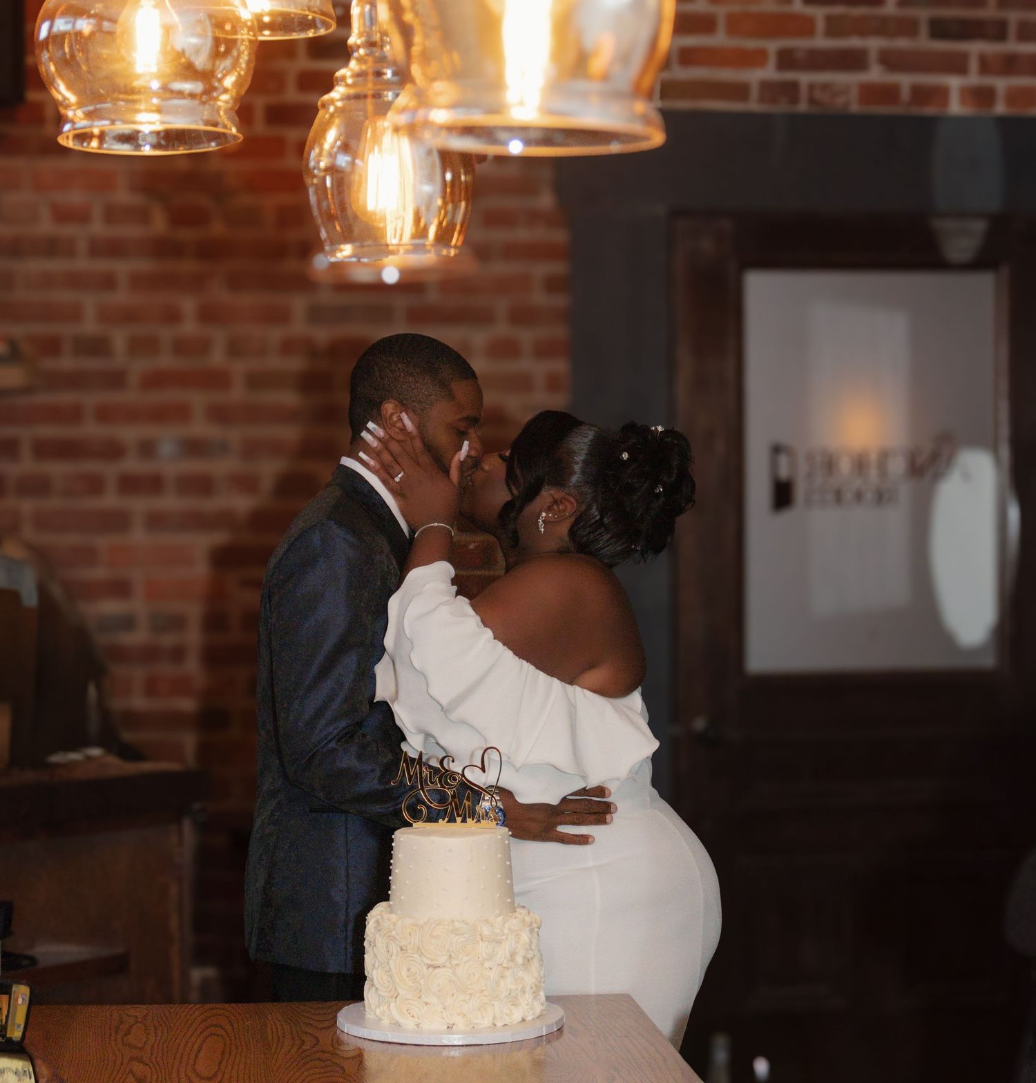 Romantic moment between newlyweds during reception with wedding cake and warm lighting.